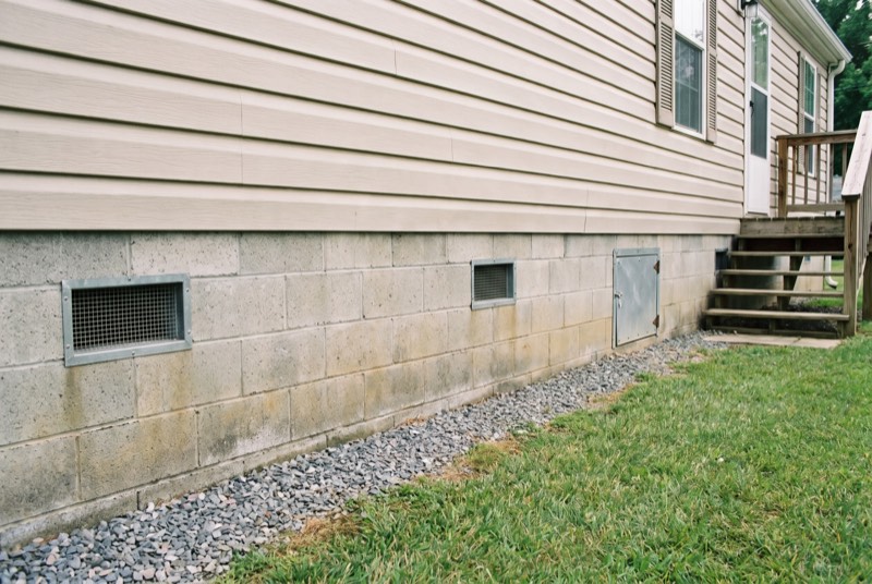 A manufactured home on a concrete block foundation wall with vents and a crawl space door